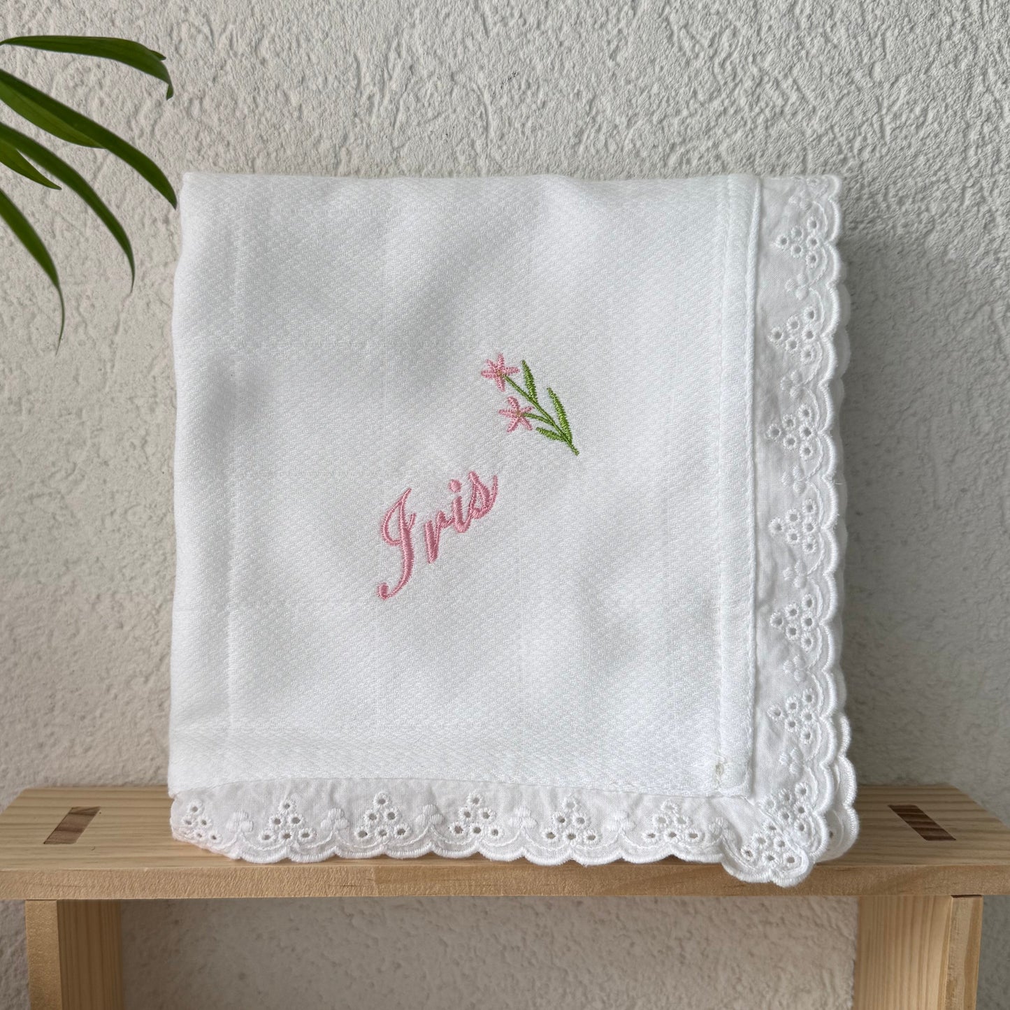White embroidered baby diaper on a wooden stand with a plant in the background