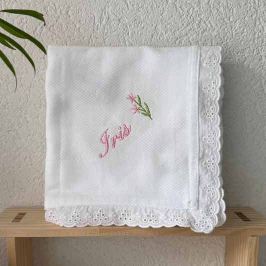 White embroidered baby diaper on a wooden stand with a plant in the background