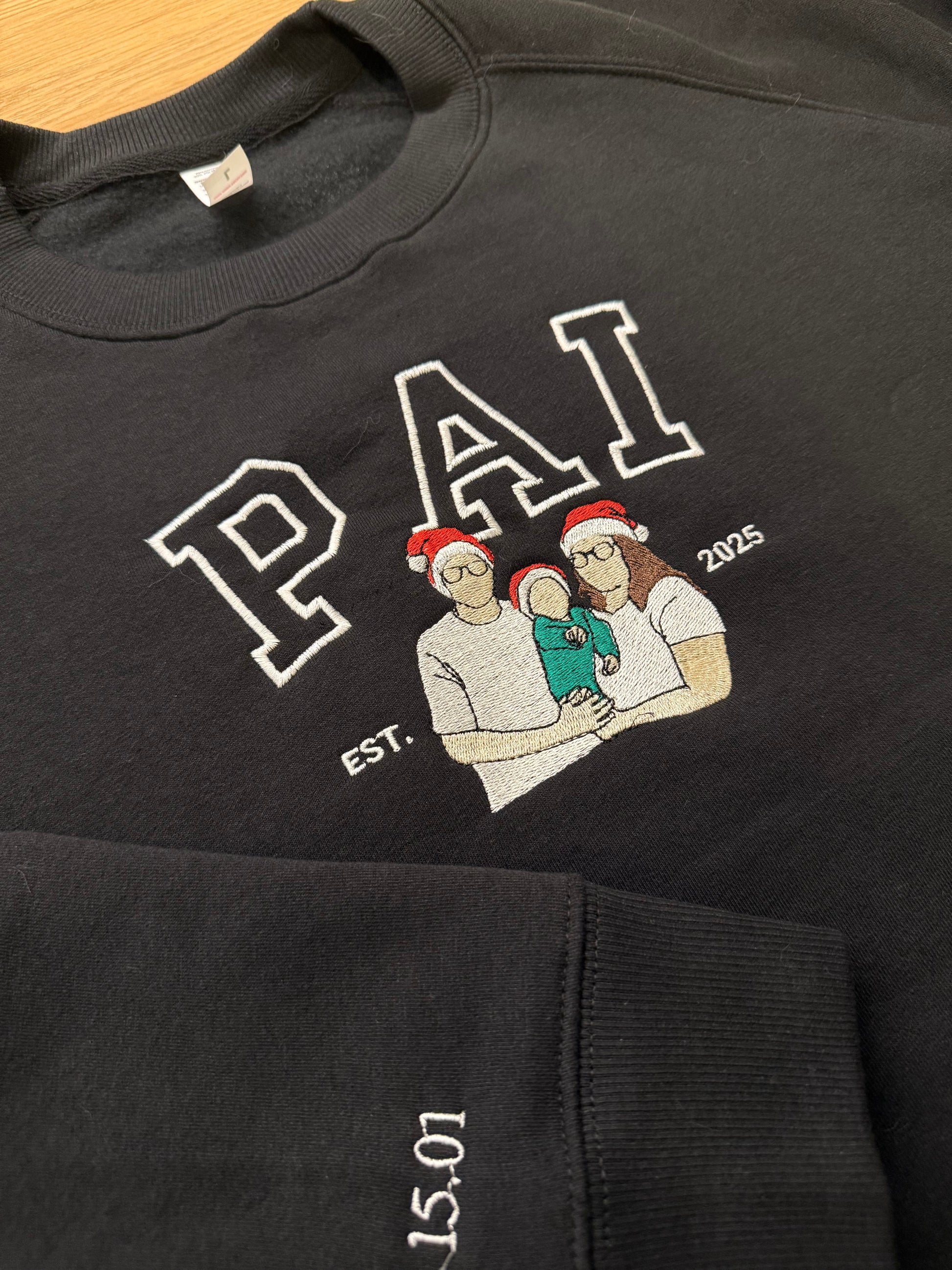 Black sweatshirt with embroidered design and text on a wooden surface