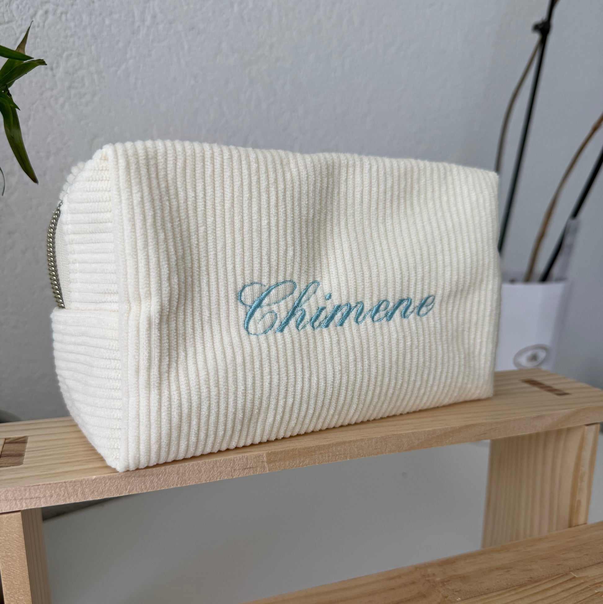 White corduroy pouch with 'Chimene' embroidery on a wooden surface.